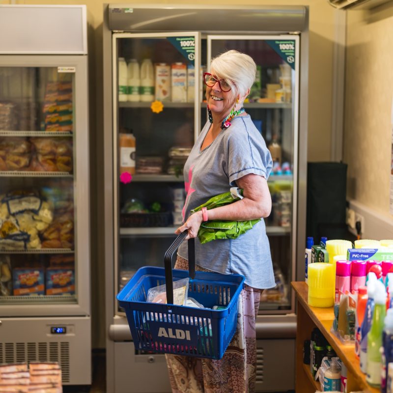 A lady holding a blue basket full of food